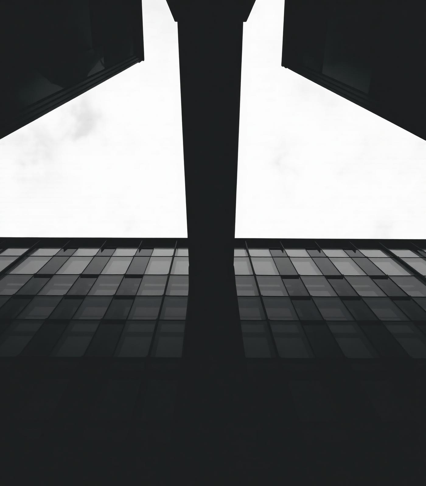Upward view of a monochrome geometric glass building against overcast sky